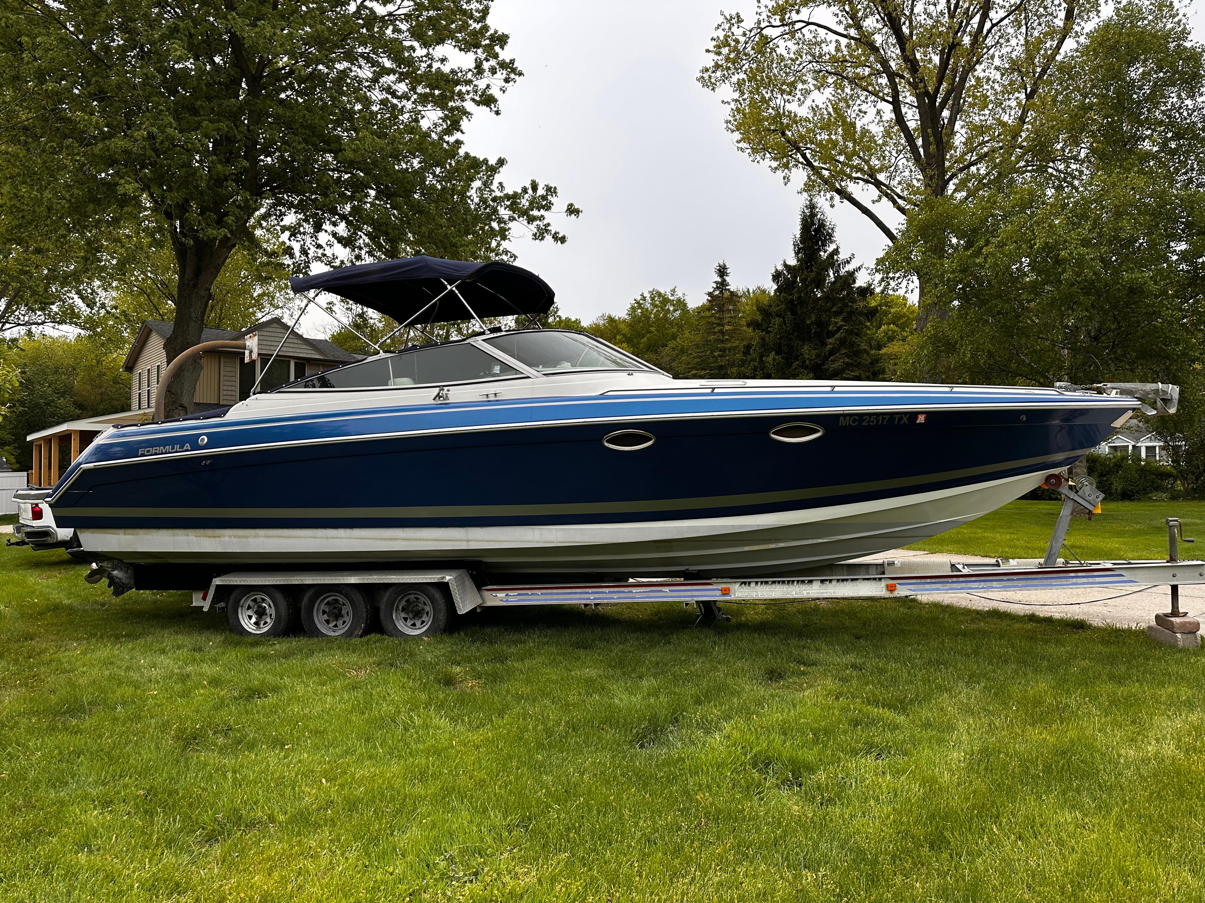 1998 Formula 330 Sun Sport boat on trailer, parked on grass with trees in background.